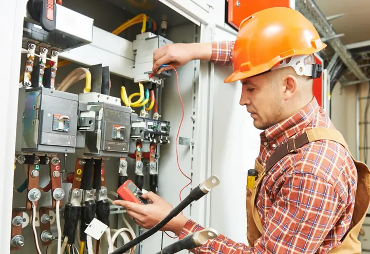Électricien mesurant au multimètre les départs d'une armoire électrique de puissance