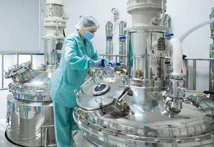 Opératrice en tenue de salle blanche intervenant sur des cuves de procédé en inox
